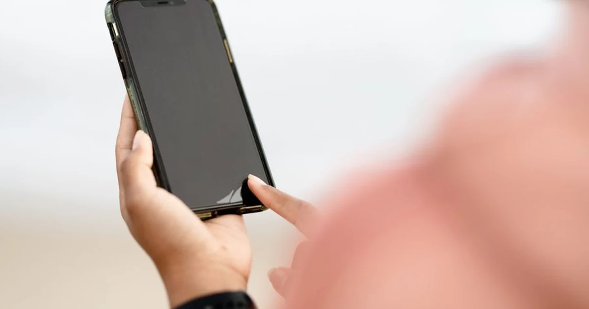 Two hands holding a phone up in bright daylight on a street